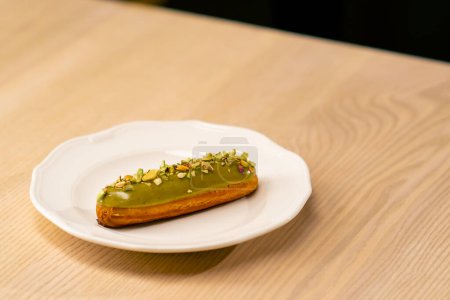 Foto de Un primer plano de un postre de eclair con pistachos acostados en un plato blanco en un restaurante italiano - Imagen libre de derechos