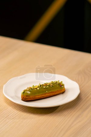 Foto de Un primer plano de un postre de eclair con pistachos acostados en un plato blanco en un restaurante italiano - Imagen libre de derechos