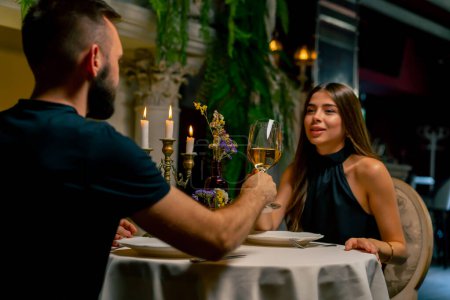 Photo for Young couple guy and girl sitting in an Italian restaurant sweetly chatting and drinking wine while on date - Royalty Free Image