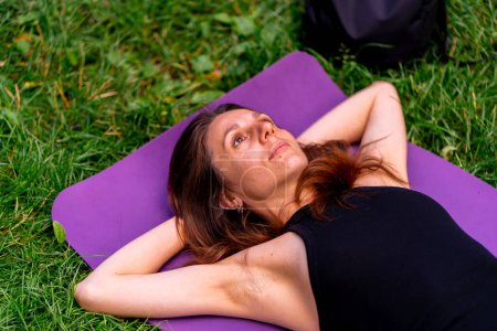 Photo for Active beautiful yogi woman resting in the city park after training lying on a fitness mat looking at sky - Royalty Free Image