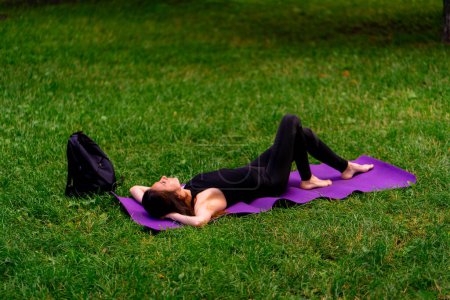 Photo for Active beautiful yogi woman resting in the city park after training lying on a fitness mat looking at sky - Royalty Free Image