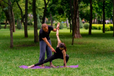 Photo for A male yoga instructor conducts a class with a woman in the park in fresh air couple exercises spiritual practices - Royalty Free Image