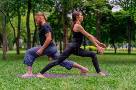 Téléchargez les photos : Couple en amour ou instructeur de yoga et femme faisant des exercices dans le parc de la ville asana pratique spirituelle corps sain étirement muscles - en image libre de droit