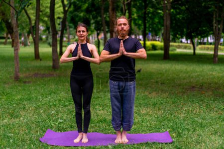 Photo for Couple practicing yoga outdoors in a city park doing meditation exercises with namaste gestures people focus mental and spiritual health - Royalty Free Image