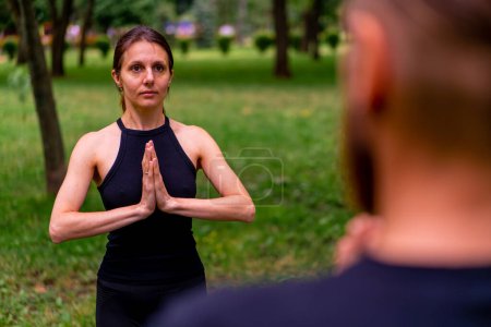 Foto de Pareja practicando yoga al aire libre en un parque de la ciudad haciendo ejercicios de meditación con gestos namaste las personas se centran en la salud mental y espiritual - Imagen libre de derechos