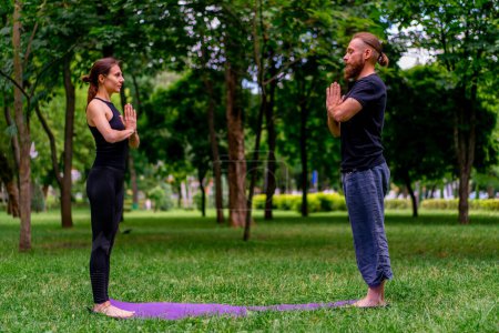 Téléchargez les photos : Couple pratiquant le yoga à l'extérieur dans un parc de la ville faire des exercices de méditation avec des gestes namaste les gens se concentrent sur la santé mentale et spirituelle - en image libre de droit