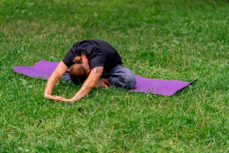 Téléchargez les photos : Bel homme barbu méditant dans le parc pratiquant le yoga faisant des étirements et des exercices différents groupes musculaires - en image libre de droit