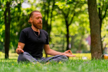 Photo for Portrait handsome bearded man meditating in the park sitting in lotus position practicing yoga zen healthy lifestyle calm meditation - Royalty Free Image