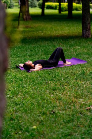 Téléchargez les photos : Active belle femme yogi reposant dans le parc de la ville après l'entraînement couché sur un tapis de fitness en regardant le ciel - en image libre de droit