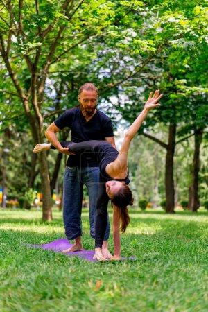 Photo for A male yoga instructor conducts a class with a woman in the park in fresh air couple exercises spiritual practices - Royalty Free Image
