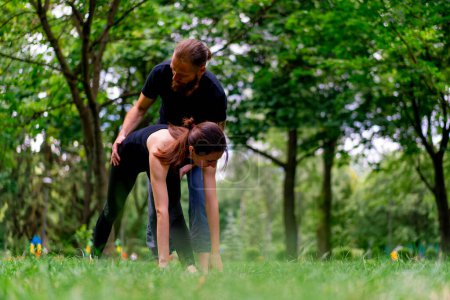Foto de Un instructor de yoga masculino conduce una clase con una mujer en el parque en pareja de aire fresco ejercita prácticas espirituales - Imagen libre de derechos