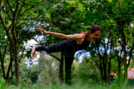 Foto de Una instructora experimentada medita en el parque practica yoga hace estiramientos y ejercita diferentes grupos musculares - Imagen libre de derechos