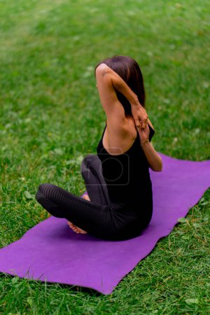 Foto de Una instructora experimentada medita en el parque practica yoga hace estiramientos y ejercita diferentes grupos musculares - Imagen libre de derechos