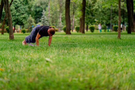 Photo for Handsome bearded man meditating in the park practicing yoga doing stretching and exercises different muscle groups - Royalty Free Image