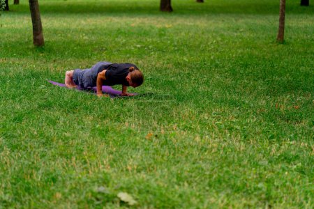 Téléchargez les photos : Bel homme barbu méditant dans le parc pratiquant le yoga faisant des étirements et des exercices différents groupes musculaires - en image libre de droit