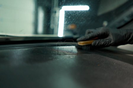 Téléchargez les photos : Gros plan d'un ouvrier de lavage de voiture utilisant une brosse et des produits chimiques pour nettoyer le tableau de bord d'une voiture de luxe pendant le processus de détail - en image libre de droit