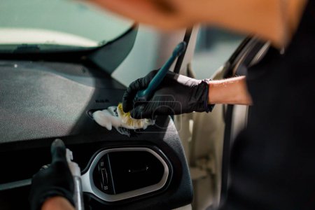 Foto de Un primer plano de un trabajador de lavado de coches utilizando un cepillo y productos químicos para limpiar el tablero de instrumentos de un coche de lujo durante el proceso de detalle - Imagen libre de derechos