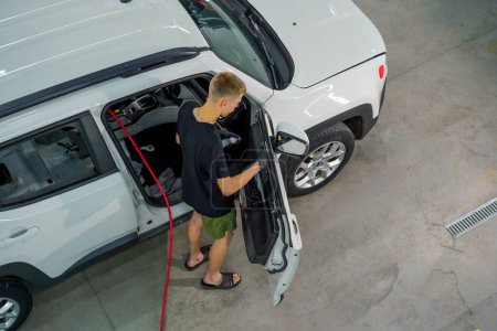 Téléchargez les photos : Travailleur de lavage de voiture de vue supérieure utilise une brosse et mousse de lavage de voiture pour laver une carte de porte de voiture de luxe pendant le processus de détails - en image libre de droit