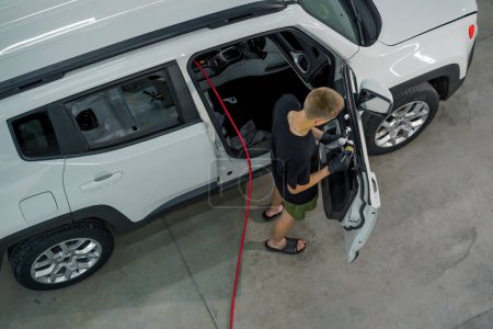 Foto de Vista superior trabajador de lavado de coches utiliza un cepillo y espuma de lavado de coches para lavar una tarjeta de puerta de coche de lujo durante el proceso de detalle - Imagen libre de derechos