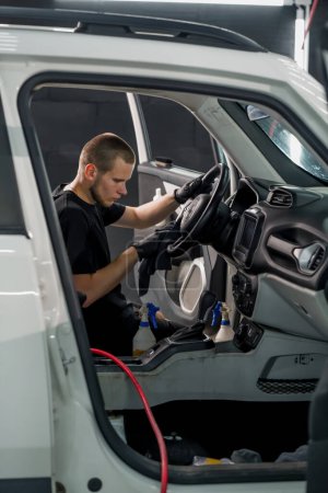 Foto de Primer plano de un trabajador de lavado de coches limpiando el volante de un coche de lujo con un cepillo y espuma de lavado en proceso de desenredar - Imagen libre de derechos