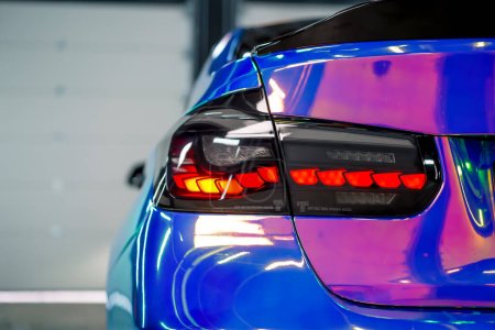 Téléchargez les photos : Gros plan sur le phare arrière d'une voiture de luxe en pellicule couleur caméléon dans le processus de détails de voiture - en image libre de droit