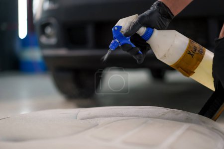 Photo for Close-up of a car wash worker applying car wash chemical with a spray gun to car crosses removed from a luxury car in process of detailing - Royalty Free Image