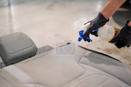 Photo for Close-up of a car wash worker applying car wash chemical with a spray gun to car crosses removed from a luxury car in process of detailing - Royalty Free Image