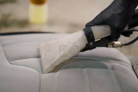 Photo for A close-up of car wash worker using a vacuum cleaner to clean white car seats in the process of detangling - Royalty Free Image