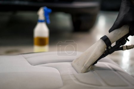 Photo for A close-up of car wash worker using a vacuum cleaner to clean white car seats in the process of detangling - Royalty Free Image