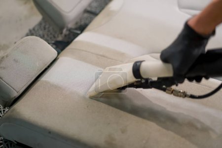 Téléchargez les photos : Gros plan d'un ouvrier de lavage de voiture utilisant un aspirateur pour nettoyer les sièges d'auto blancs en cours de démêlage - en image libre de droit