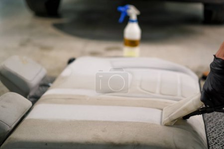 Téléchargez les photos : Gros plan d'un ouvrier de lavage de voiture utilisant un aspirateur pour nettoyer les sièges d'auto blancs en cours de démêlage - en image libre de droit