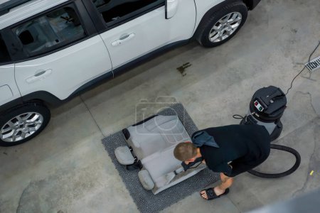 Foto de Un trabajador de lavado de coches utiliza una aspiradora para limpiar asientos de coche blancos en proceso de desenredar la vista superior - Imagen libre de derechos