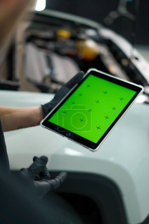 Téléchargez les photos : Deux mécaniciens automobiles se tiennent à côté du VUS blanc avec le capot ouvert et regardent une tablette avec un écran vert ouvert tout en réparant la voiture - en image libre de droit