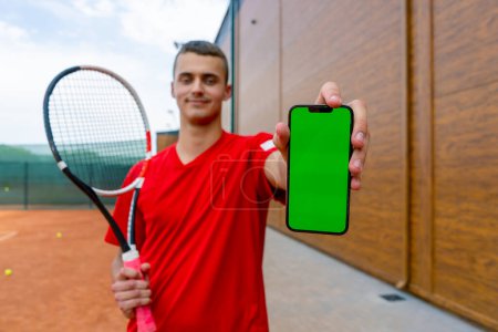 Téléchargez les photos : Portrait de jeune joueur de tennis professionnel après l'entraînement court de tennis avec raquette dans les mains montre téléphone avec écran vert - en image libre de droit