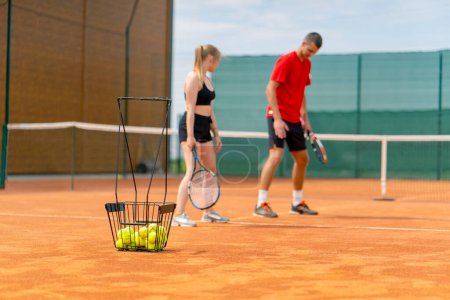 Foto de Un joven entrenador enseña a una chica principiante a jugar al tenis, practicar movimientos con raqueta practicar con una pelota en una cancha de tenis - Imagen libre de derechos