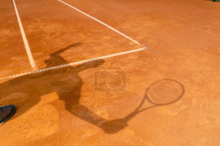 Téléchargez les photos : L'ombre d'un joueur de tennis ou d'un entraîneur sur un terrain de sport ouvert en terre battue orange - en image libre de droit