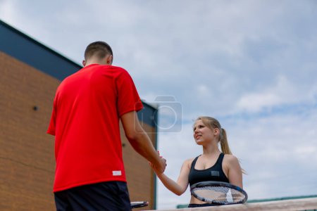 Téléchargez les photos : Jeune homme et femme serrant la main avant le début d'un match de tennis sur terrain ouvert joueurs sportifs adversaires - en image libre de droit