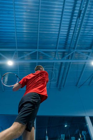 Téléchargez les photos : Jeune homme sur un court de tennis intérieur frapper la balle avec une raquette dans un service de saut pendant le sport professionnel instructeur de tennis de jeu - en image libre de droit