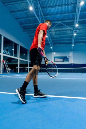 Téléchargez les photos : Jeune homme sur un court de tennis intérieur frappant la balle avec une raquette servant pendant le sport professionnel instructeur de tennis de match - en image libre de droit