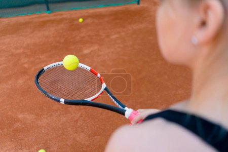 Foto de Joven chica principiante tenista golpeando la pelota con una raqueta en la cancha practicando y aprendiendo a golpear y servir deporte hobby primer plano - Imagen libre de derechos