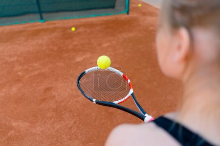 Foto de Joven chica principiante tenista golpeando la pelota con una raqueta en la cancha practicando y aprendiendo a golpear y servir deporte hobby primer plano - Imagen libre de derechos