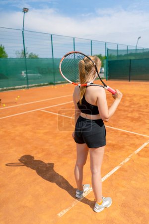 Téléchargez les photos : Portrait d'une jeune fille souriante avant de jouer au tennis sur le terrain avec raquette dans ses mains passe-temps jeu entraînement championnat sport vue arrière - en image libre de droit