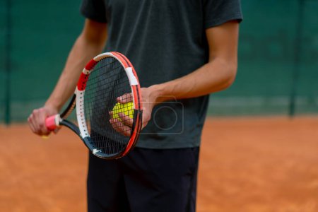 Foto de Joven entrenador o jugador sosteniendo raqueta de tenis y pelota mientras juega en primer plano de la cancha - Imagen libre de derechos