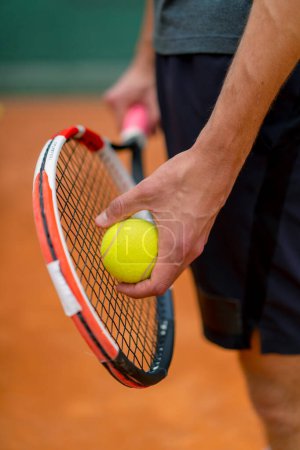 Téléchargez les photos : Jeune entraîneur ou joueur tenant raquette de tennis et ballon tout en jouant sur le terrain gros plan - en image libre de droit
