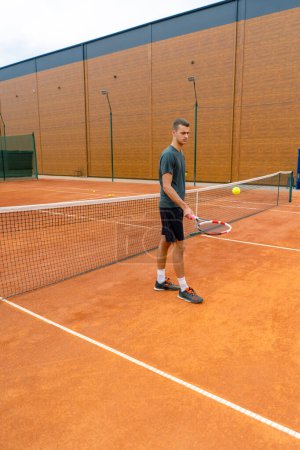 Foto de Joven entrenador de tenis golpeando la pelota con una raqueta en la cancha de tenis preparándose para el estilo de vida deportivo de competición - Imagen libre de derechos
