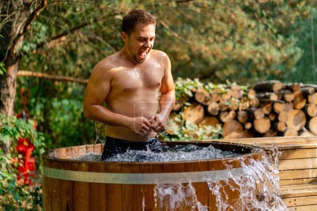 Téléchargez les photos : Beau sportif souriant homme relaxant dans l'eau froide dans une piscine extérieure dans la nature dans les bois - en image libre de droit