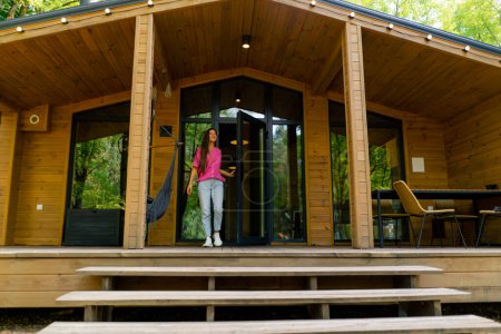 Photo for A slim smiling girl walks out in the morning on the terrace of her wooden cabin in the woods - Royalty Free Image