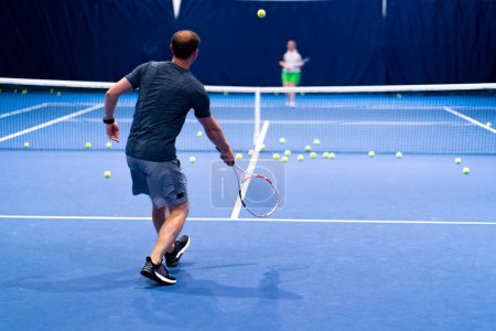 Téléchargez les photos : Un homme sur un court de tennis fermé bleu avec une raquette dévie les coups de l'adversaire veut constamment gagner - en image libre de droit