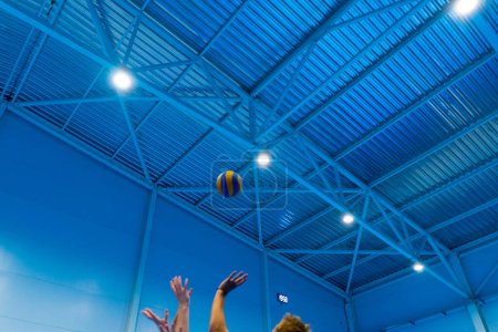 Foto de Una pelota de voleibol en el aire vuela sobre la red y vuela a una parte de los oponentes que están tratando de repeler con sus manos juego de competición - Imagen libre de derechos