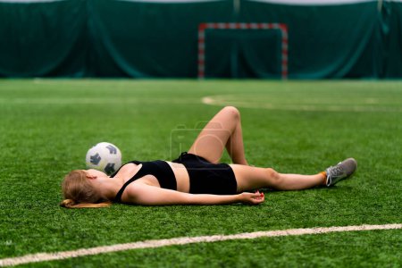 Photo for Women's soccer tired female soccer player lying resting green synthetic grass field after hard training or match - Royalty Free Image